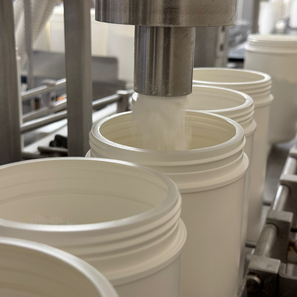A machine placing high-quality wellness powder into a white bottle.